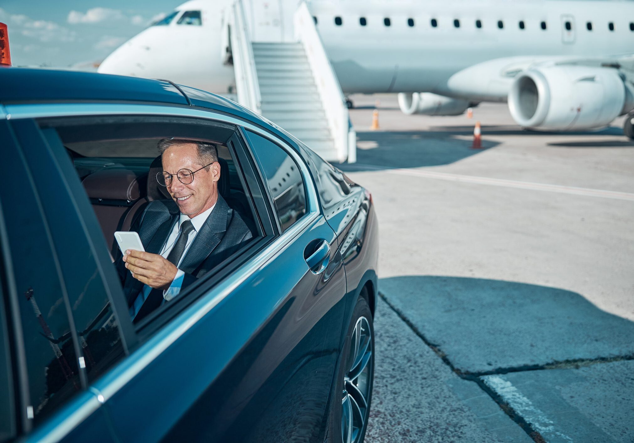 Man in car smiling at phone, airplane background.