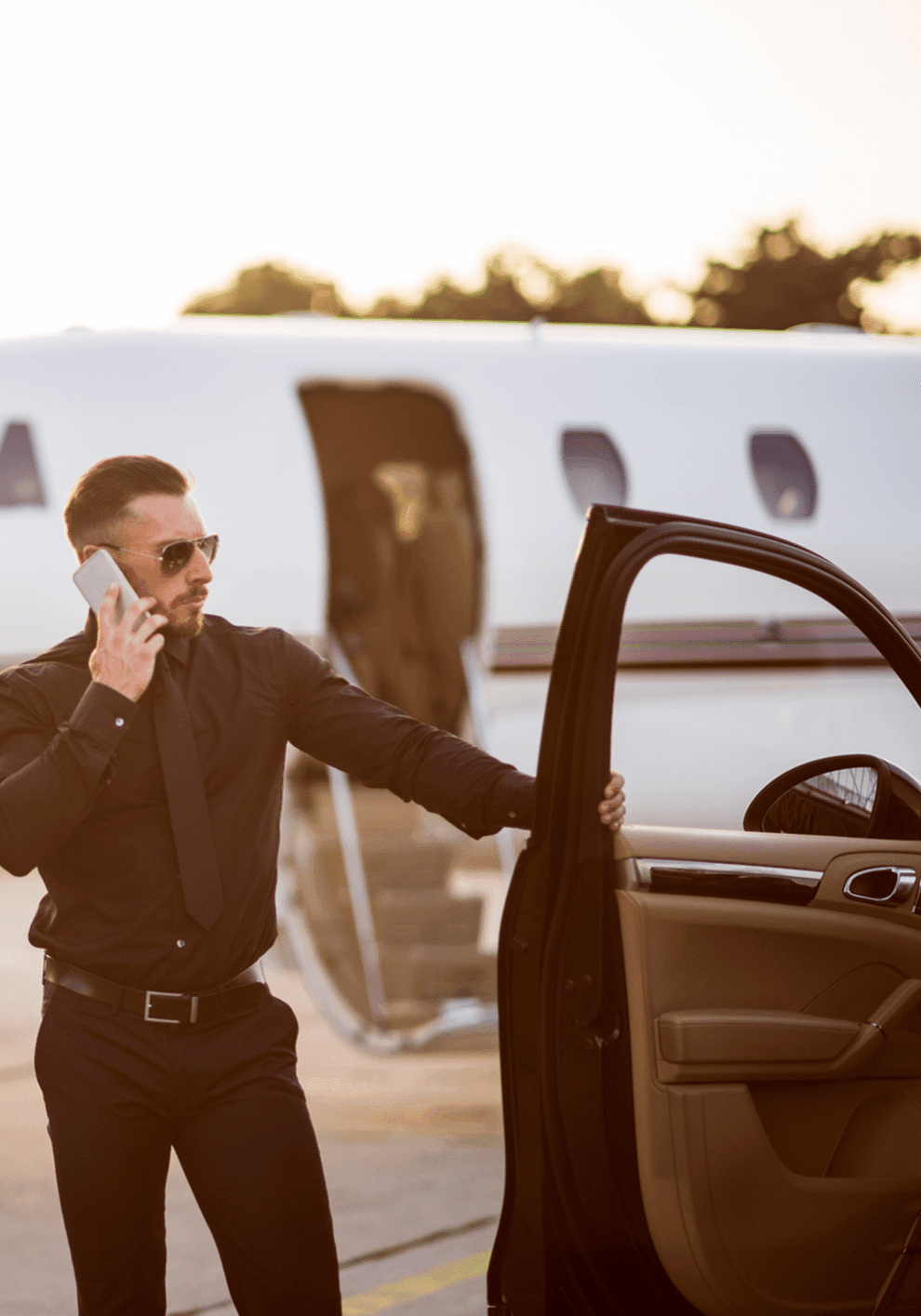 Man on phone near private jet and car.